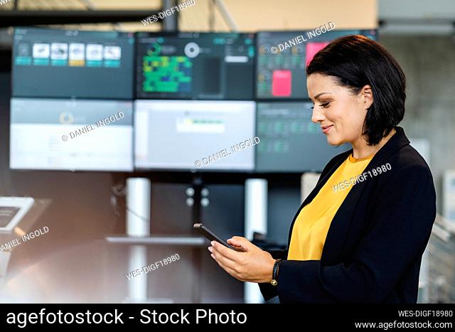 Smiling businesswoman using smart phone in front of computer monitors