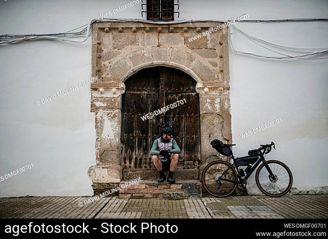 Cyclist with bicycle sitting in front of old door