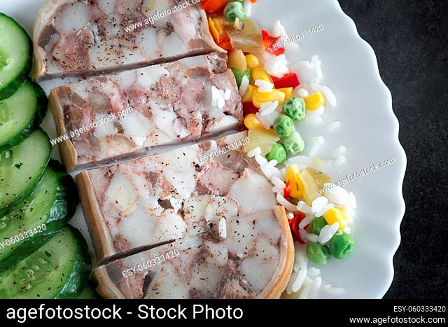 On the table on a plate of delicious meat appetizer: stuffed with meat and bacon pork stomach, sliced, next to vegetables and fresh cucumbers
