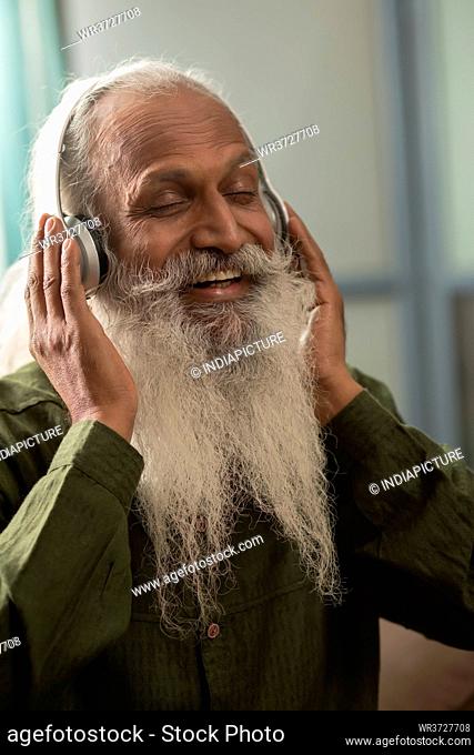 A BEARDED OLD MAN HAPPILY LISTENING TO MUSIC ON HEADPHONES