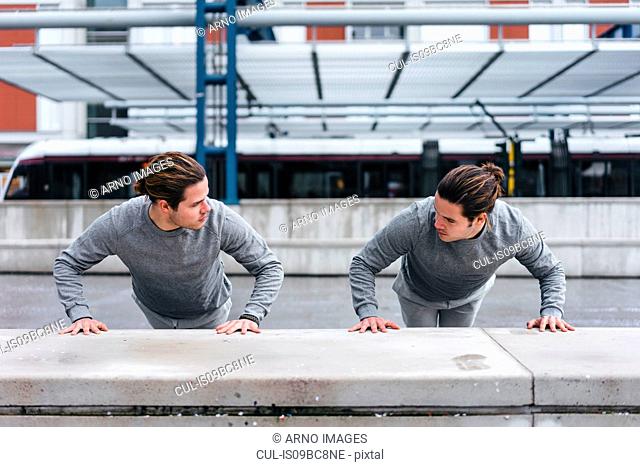 Young male twins doing push ups against wall in city