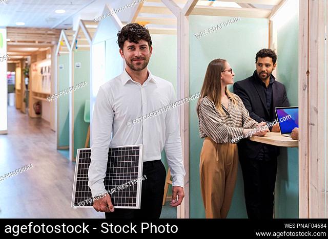 Businessman holding solar panel in office with colleagues in background