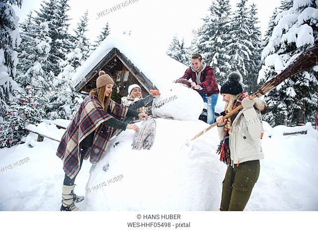 Austria, Altenmarkt-Zauchensee, friends building up big snowman at wooden house