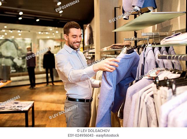 sale, shopping, fashion, style and people concept - happy young man in shirt choosing jacket in mall or clothing store