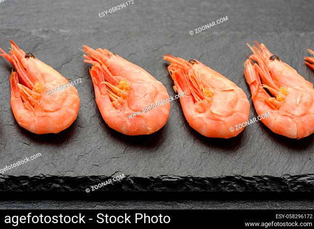 fresh shrimp in a row on a black slate board, close up