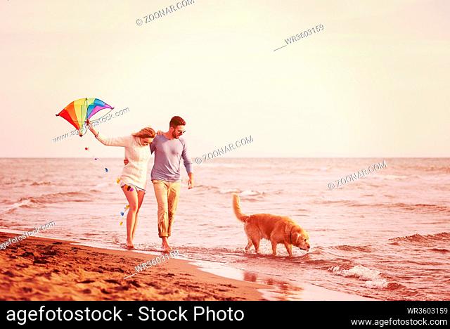 Young Couple having fun playing with a dog and Kite on the beach at autumn day filter