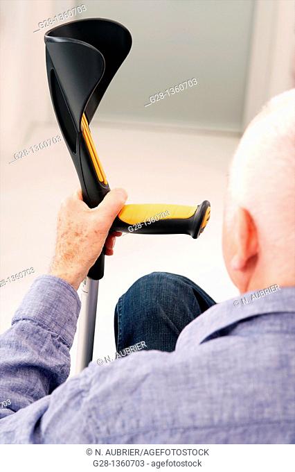 Senior man seen from behind waiting with his hand on a crutch in a clinic waiting room or medical center