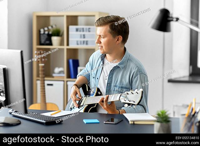 young man with computer playing guitar at home