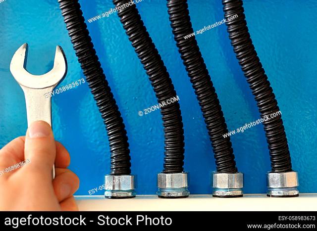 These are power cables in corrugated insulation and a rock electrician with a wrench close up against a blue wall. Reliable and correct connection of the wires...