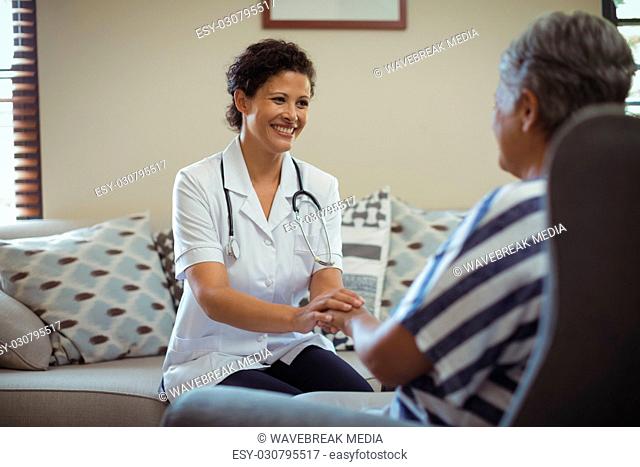 Female doctor comforting senior woman in living room