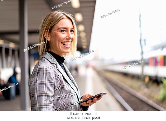 Happy young businesswoman with mobile phone at the train station