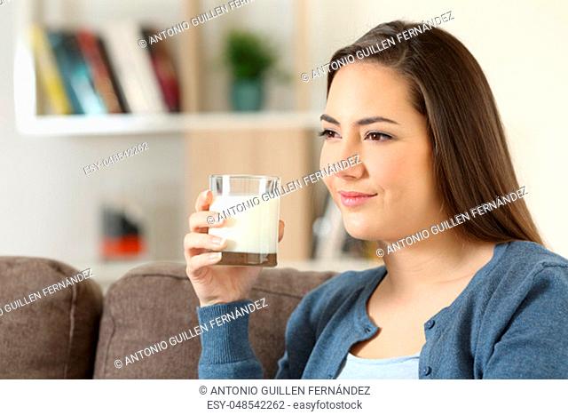 Relaxed woman holding a glass of milk sitting on a couch in the living room at home