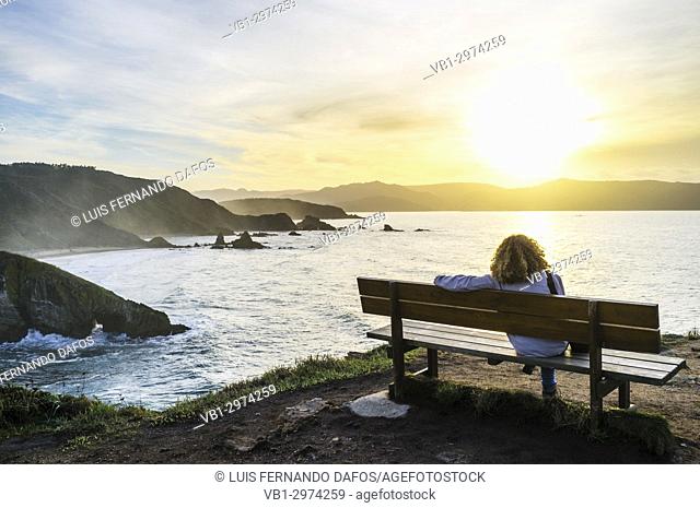 Solo woman sitting at a bench at sunset by the Loiba cliffs (Acantilados de Loiba) Coruña province, Galicia, Spain, Europe