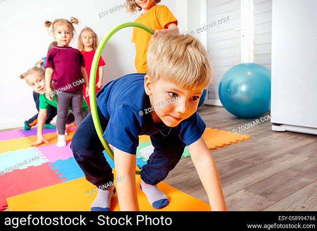Active kid crawling on colorful mats through hula hoops held by other children. Sport compeptition at kindergarten