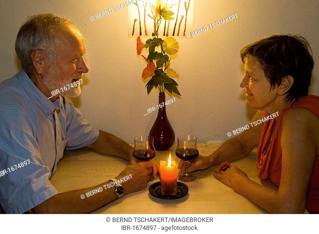 Elderly man and woman with a glass of wine by candlelight