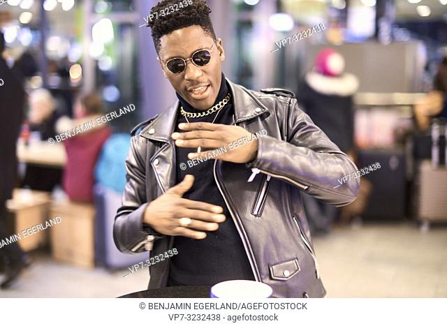 young fancy man gesticulating body language, with coffee cup at bar table, African descent, in Munich, Germany