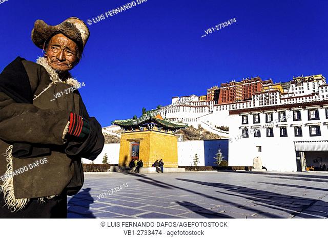 Old Tibetan man with fur hat standing in front of Potala palace in Lhasa, Tibet, China