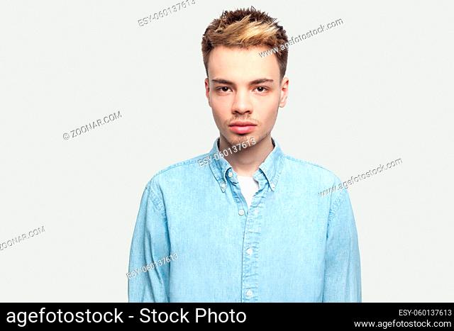 Portrait of calm serious handsome young man in light blue shirt standing and looking at camera with serious face. indoor studio shot on grey background copy...