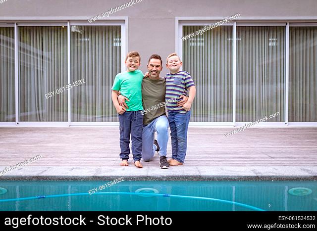 Portrait of caucasian father and two sons holding hands smiling while standing near the pool