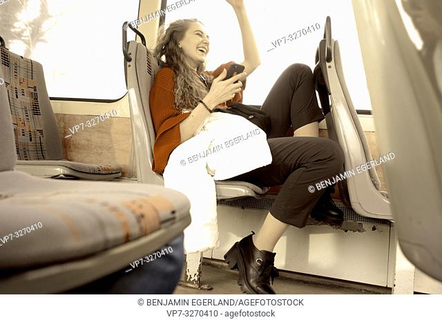 young happy laughing woman sitting in public transport with phone, in city Cottbus, Brandenburg, Germany