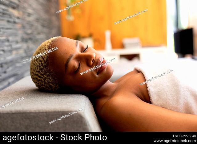 Happy african american woman wearing towel, lying with eyes closed