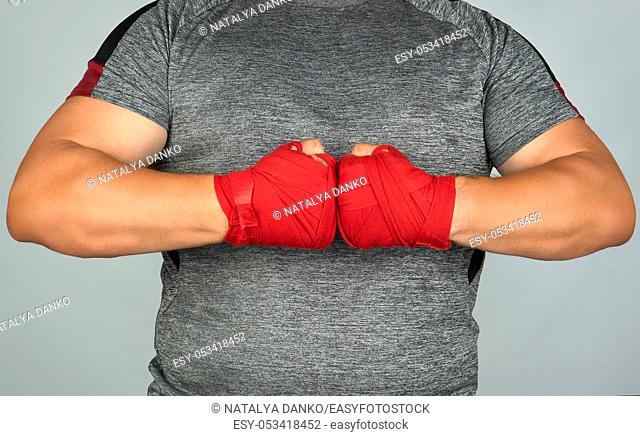 athlete in gray clothes joined his hands in front of his chest, two hands wrapped in a red textile sports bandage, white background