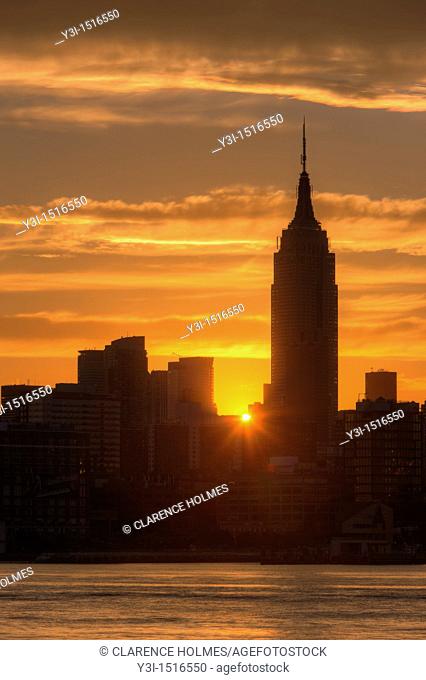 The rising sun shines between Manhattan buildings including the Empire State Building just after sunrise, New York City, New York, USA