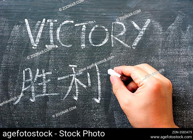 Victory - word written on a blackboard with a Chinese translation, with a hand holding chalk