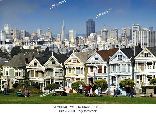 Tourists in front of Painted Ladies, Victorian, multi-coloured painted wooden houses in front of the skyline with the Transamerica Pyramid, Steiner Street
