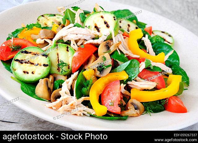 Warm chicken salad with spinach, tomato slices, sweet pepper, grilled zucchini, and champignons, all dressed with herbs and fragrant oil