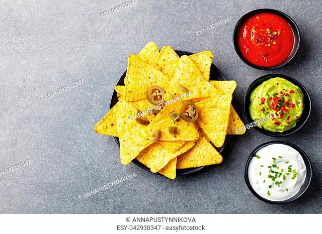 Nachos chips with dip variety on a wooden plate. Grey stone background