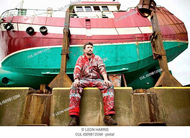 Male ship painter sitting in front of fishing boat on drydock
