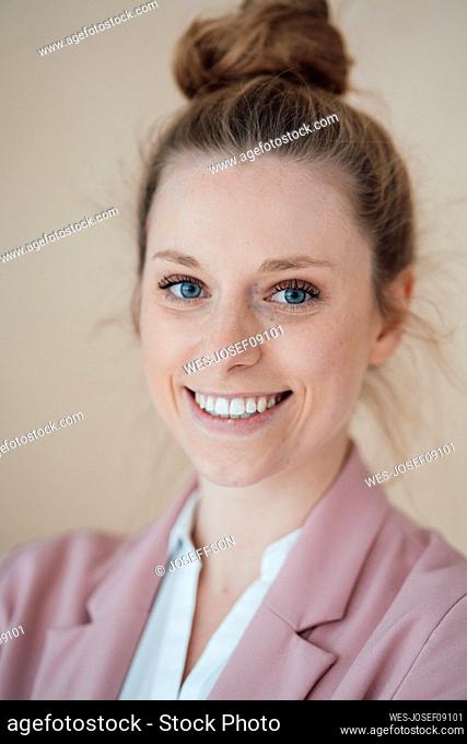 Young happy businesswoman with hair bun by wall