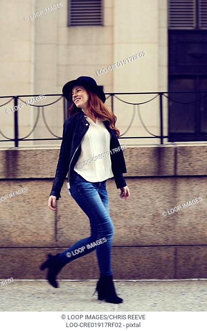 Young women in jeans and hat walking by railings in New York street