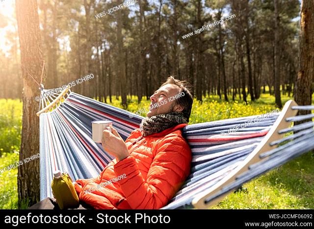 Man holding cup sitting in hammock enjoying sunny day
