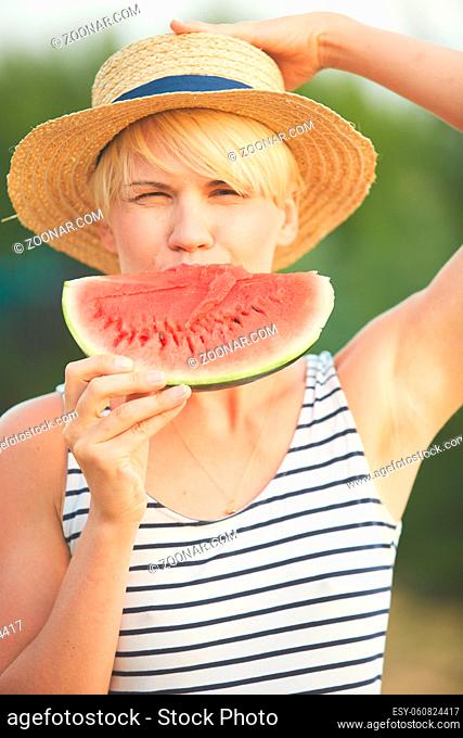 Beautiful girl in straw hat eating fresh watermelon. Film camera style