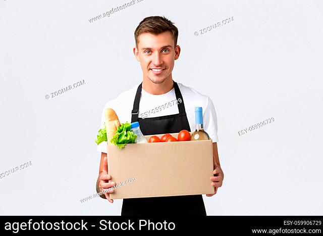 Retail, grocery shopping and delivery concept. Handsome courier in black apron handing over box with groceries, salesman prepared package for delivering company...