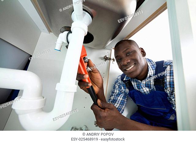 Young African Handyman Repairing Sink Pipe With Worktool