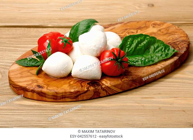 Italian cuisine. Mozzarella, heirloom tomatoes, basil leaves on a wooden serving plate. Selective focus on cheese