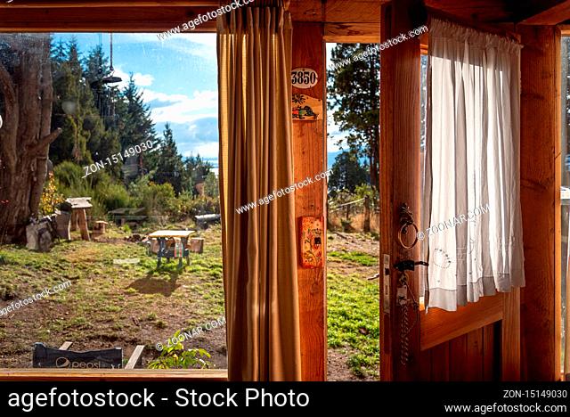 BARILOCHE, ARGENTINA, JUNE 18, 2019: An open door seen from the interior of a wooden cozy and relaxing cabin that leads to the forest and lake