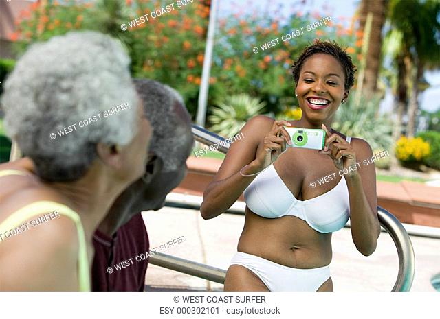 Woman wearing bikini photographing senior couple outdoors