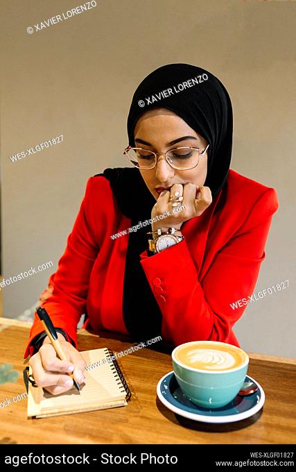 Young female entrepreneur writing on diary by coffee at cafe