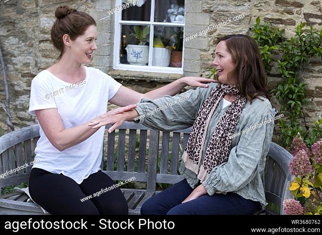 Therapist and client seated in a garden, touching the hands and shoulder