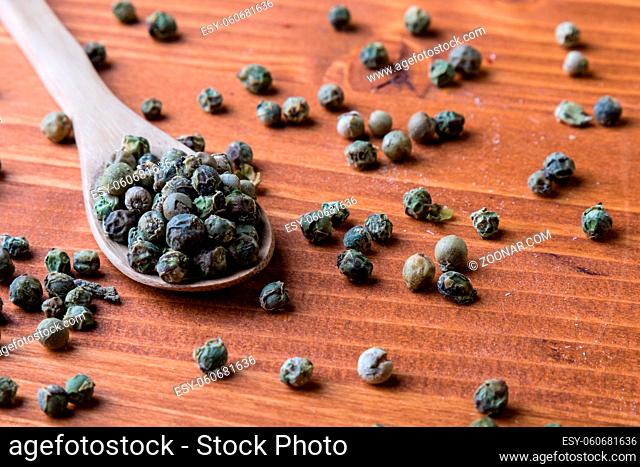 green color peppercorn seeds on wooden table with spoon