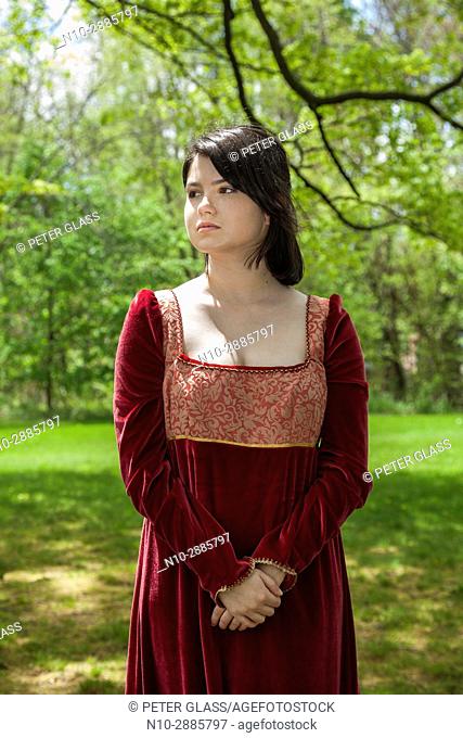 Young woman, standing in a park, wearing a long red vintage dress