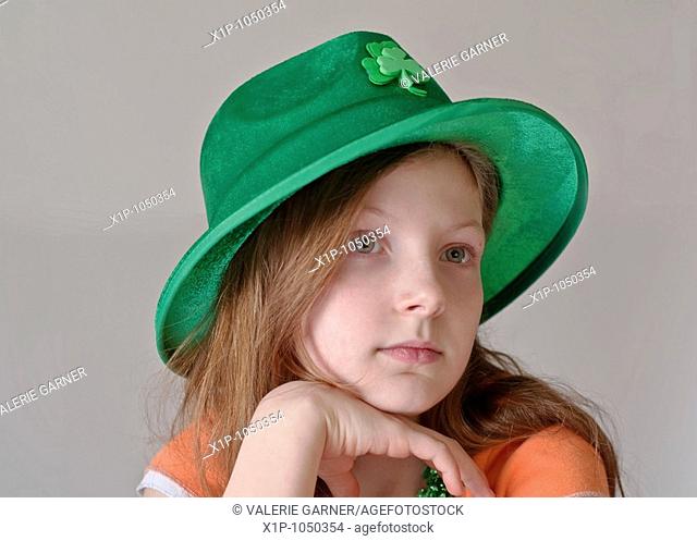 This beautiful green eyed, 9 year old Caucasian girl is wearing a green St Patrick's Day hat in a closeup on a light background Her facial expression is a more...