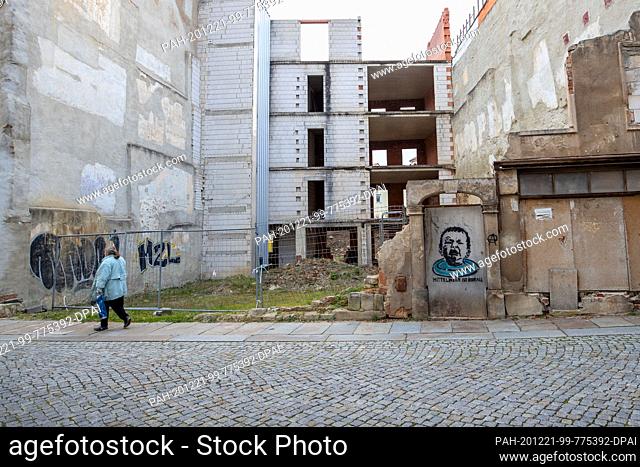 21 December 2020, Saxony, Zittau: A woman walks past an unfinished building in a side street of the market square. On a door of the construction site there is...