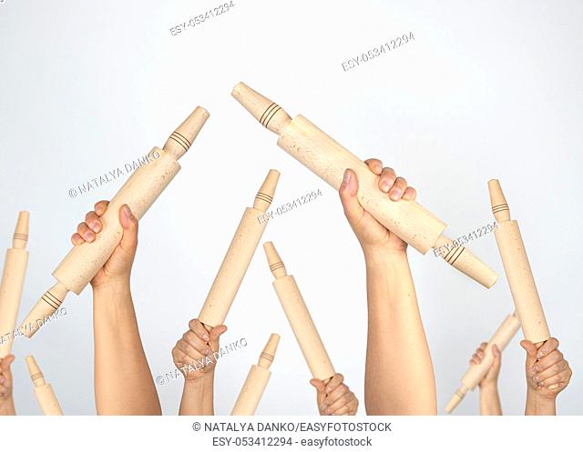 many hands raised up and holding kitchen wooden rolling pins on gray background, concept of riot