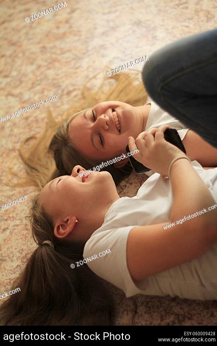 Two teen girls lying on the floor, laughing and looking at the phone, their hair spread over the floor, the concept of youth relations