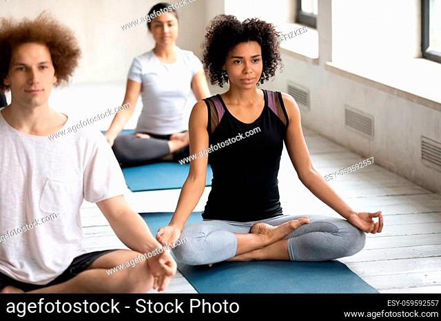 Full length young calm african ethnicity slim sporty woman sitting in lotus position, starting yoga practice or relaxing after intensive workout on floor mat at...